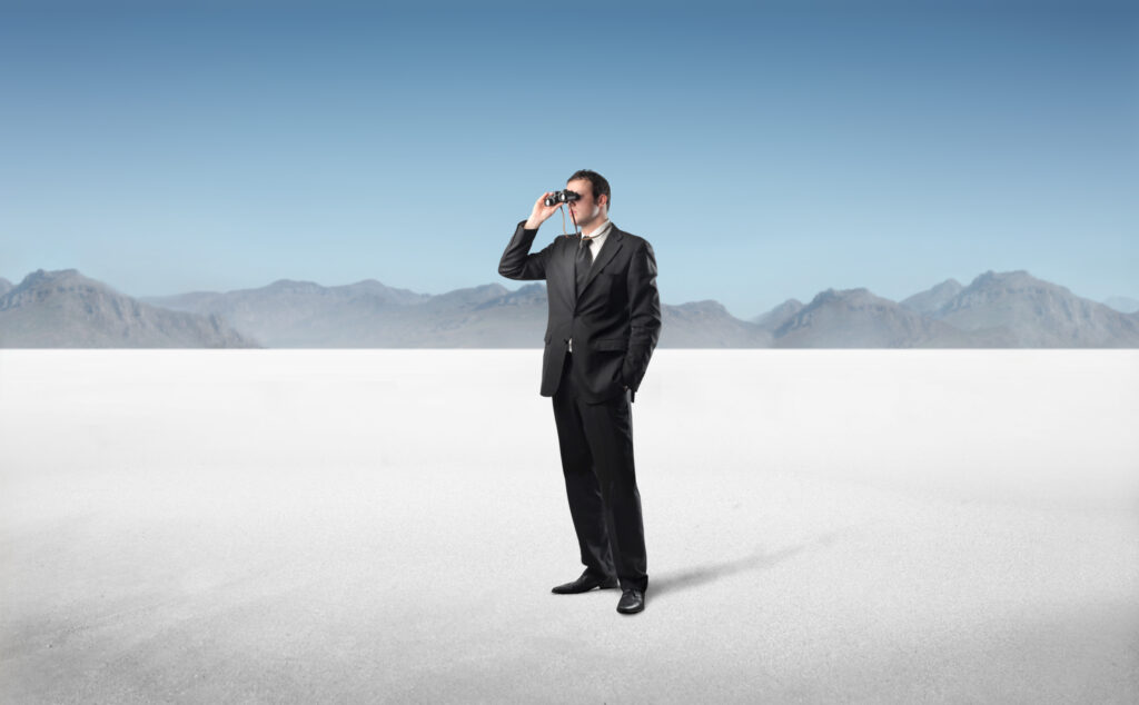 Man in a desert staring through binoculars into the distance